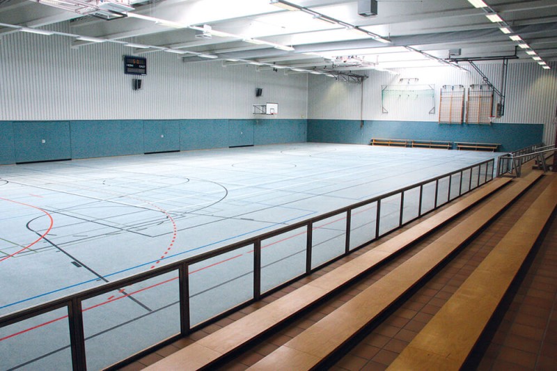 Trainingshalle von innen mit blauem Boden und Sitzbänken aus Holz