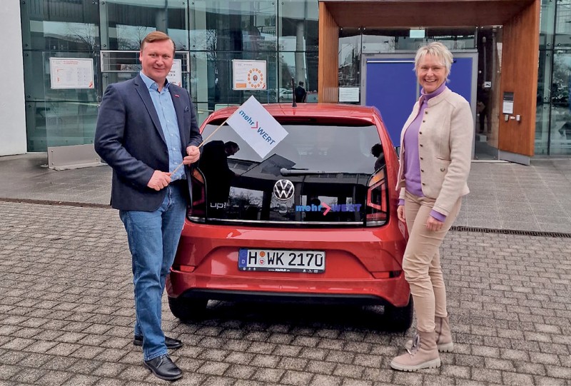 Das mehrWERT-Team in Vechta: Anjo Buschmeier und Gaby Middelbeck vor einem Auto mit Werbung.
