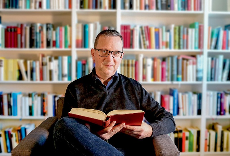 Dr. Ralf Raabe guckt in die Kamera und hält ein Buch in der Hand
