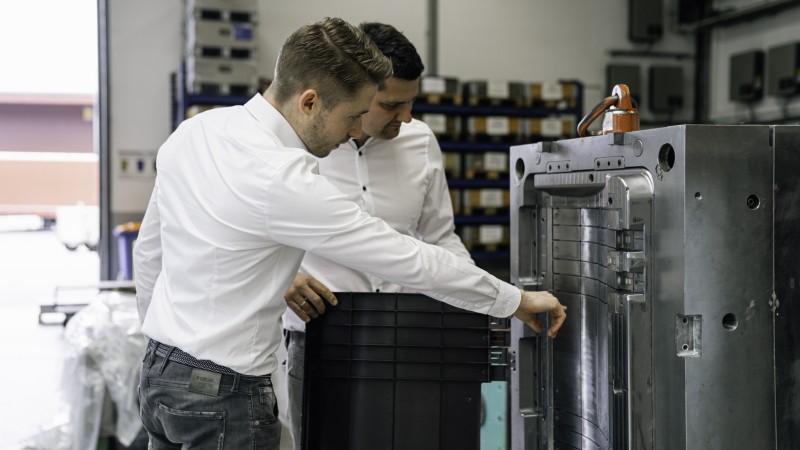 Zwei Fachkräfte prüfen ein geöffnetes Spritzgusswerkzeug in einer Produktionshalle.