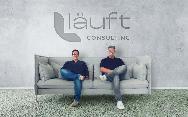 zwei Männer vor Logo auf einem Sofa