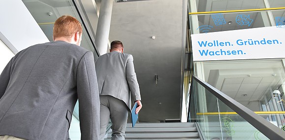 zwei Männer gehen neben Firmenlogo Treppe hinauf