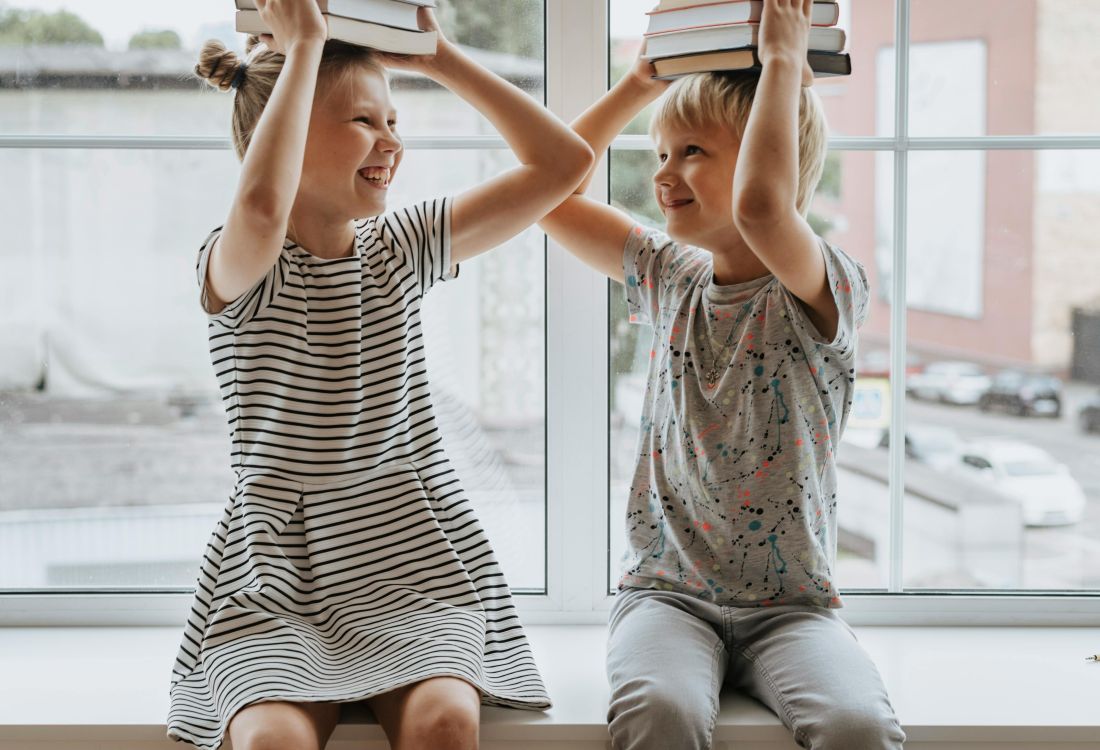2 Kinder auf einer Fensterbank mit Büchern auf dem Kopf