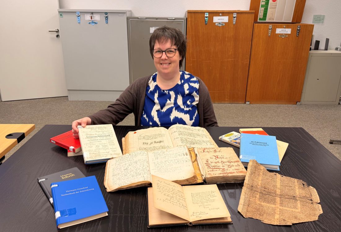 Frau sitzt vor alten Schriften, Büchern und Dokumenten