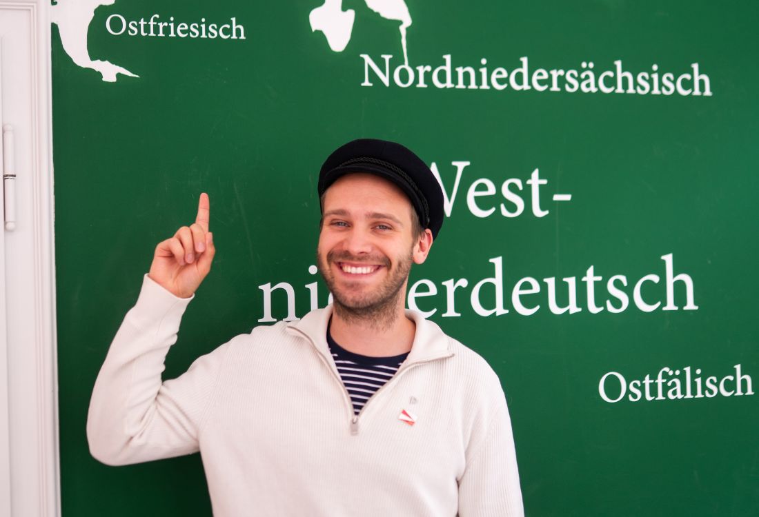 Mann steht vor einem grünen Schild und zeigt darauf