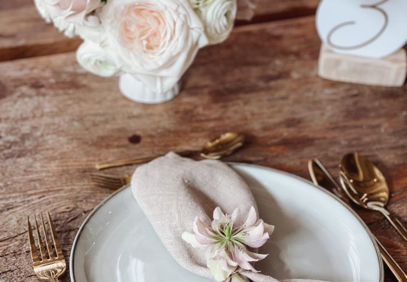 Tischdekoration für eine Hochzeit bestehend aus weißem Porzellan und goldenem Besteck mit hellen Bllüten